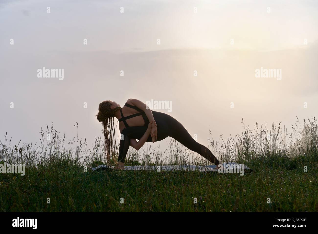 Athletic woman in sportswear doing yoga exercises during morning time among nature. Concept of people, outdoors activity and healthy lifestyles.  Stock Photo