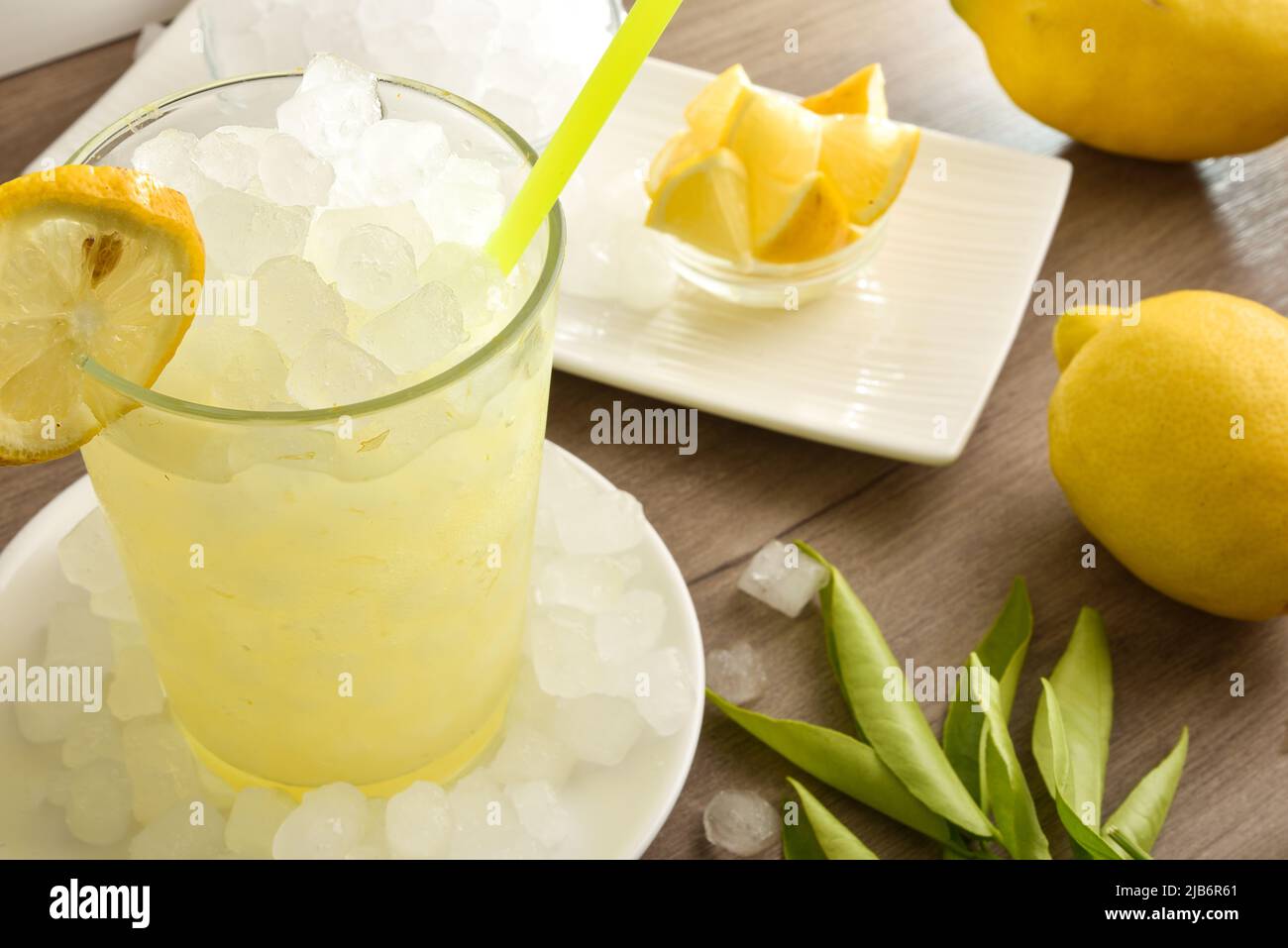 Background with detail of lemon drink with a lot of ice on  wooden table with fruit and a bowl with ice. Elevated view. Horizontal composition. Stock Photo