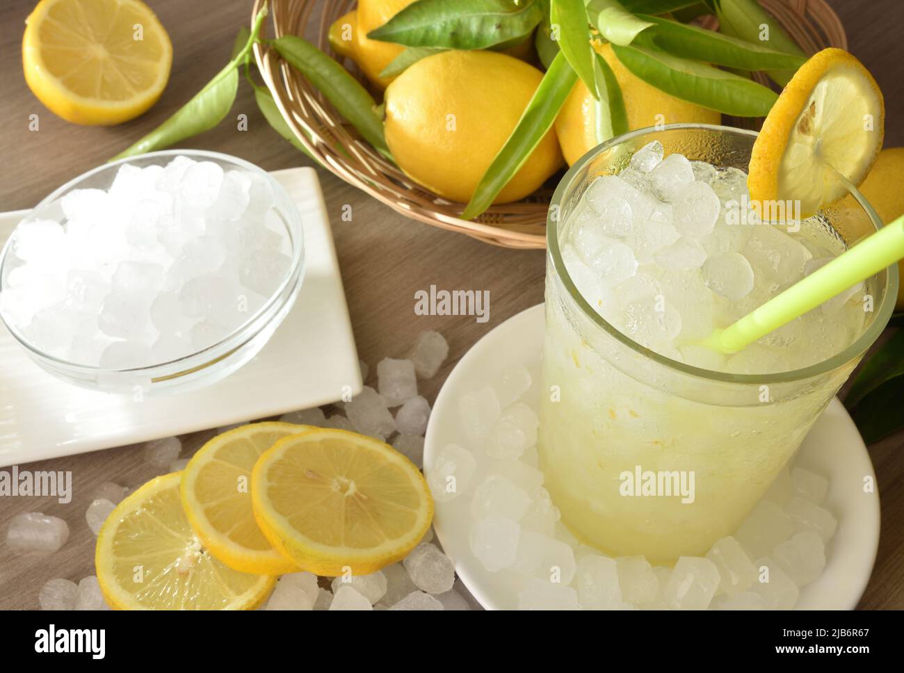 Background with lemon drink with a lot of ice in a glass on wooden table with fruit and a bowl with ice around. Top elevated view. Horizontal composit Stock Photo