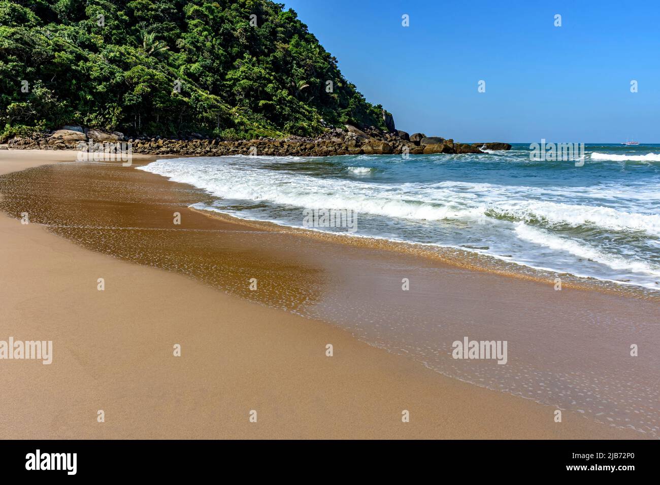 Paradisiacal rocky beach with clean and calm waters surrounded by forest and hills in Bertioga coast of Sao Paulo state, Brazil Stock Photo