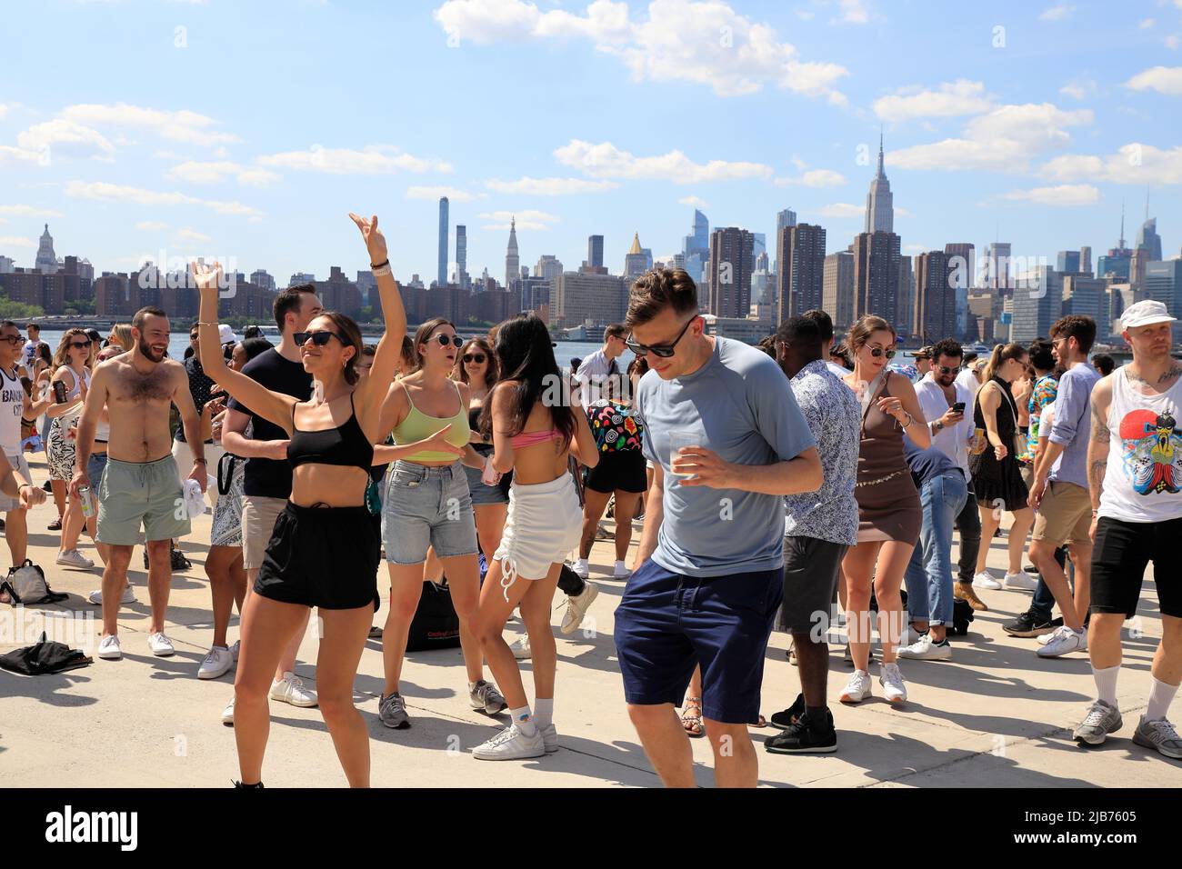 People dancing at the Hot Honey Sundays outdoor dance party in Greenpoint Terminal Market with East River and Manhattan skyline in the background.Greenpoint.Brooklyn.New York City.USA Stock Photo