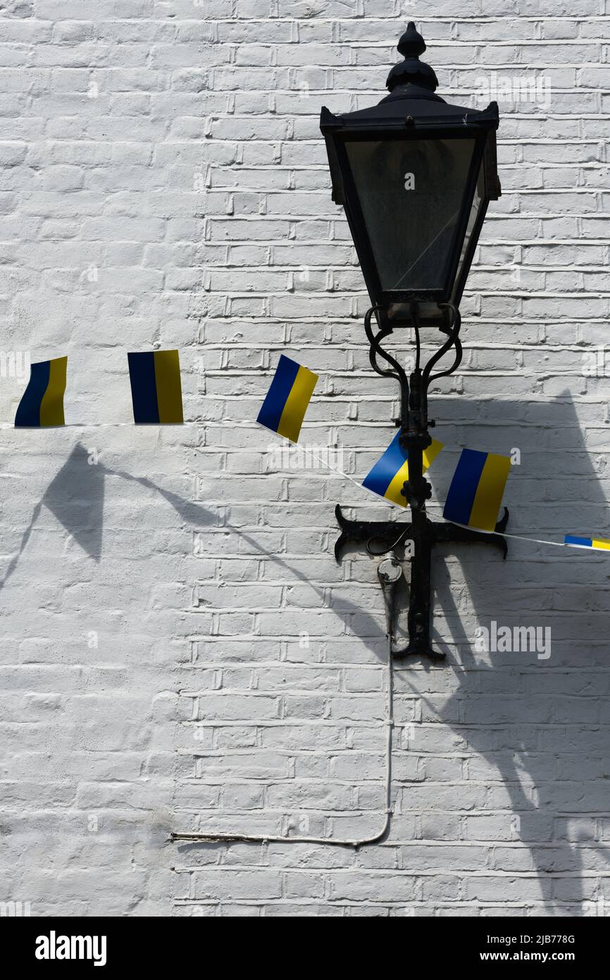 The flag of the Ukraine fdraaped over an old style English streetlight, Old Islworth, England, against a white wall with shadow Stock Photo