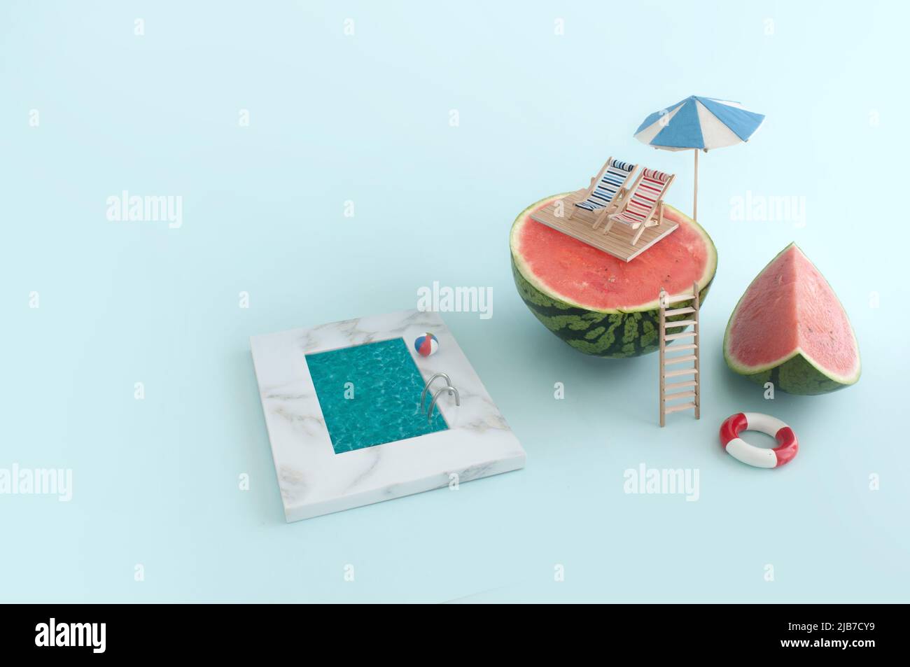 Summer vacation concept; deck chairs and beach parasol on top of a watermelon, with swimming pool down below Stock Photo