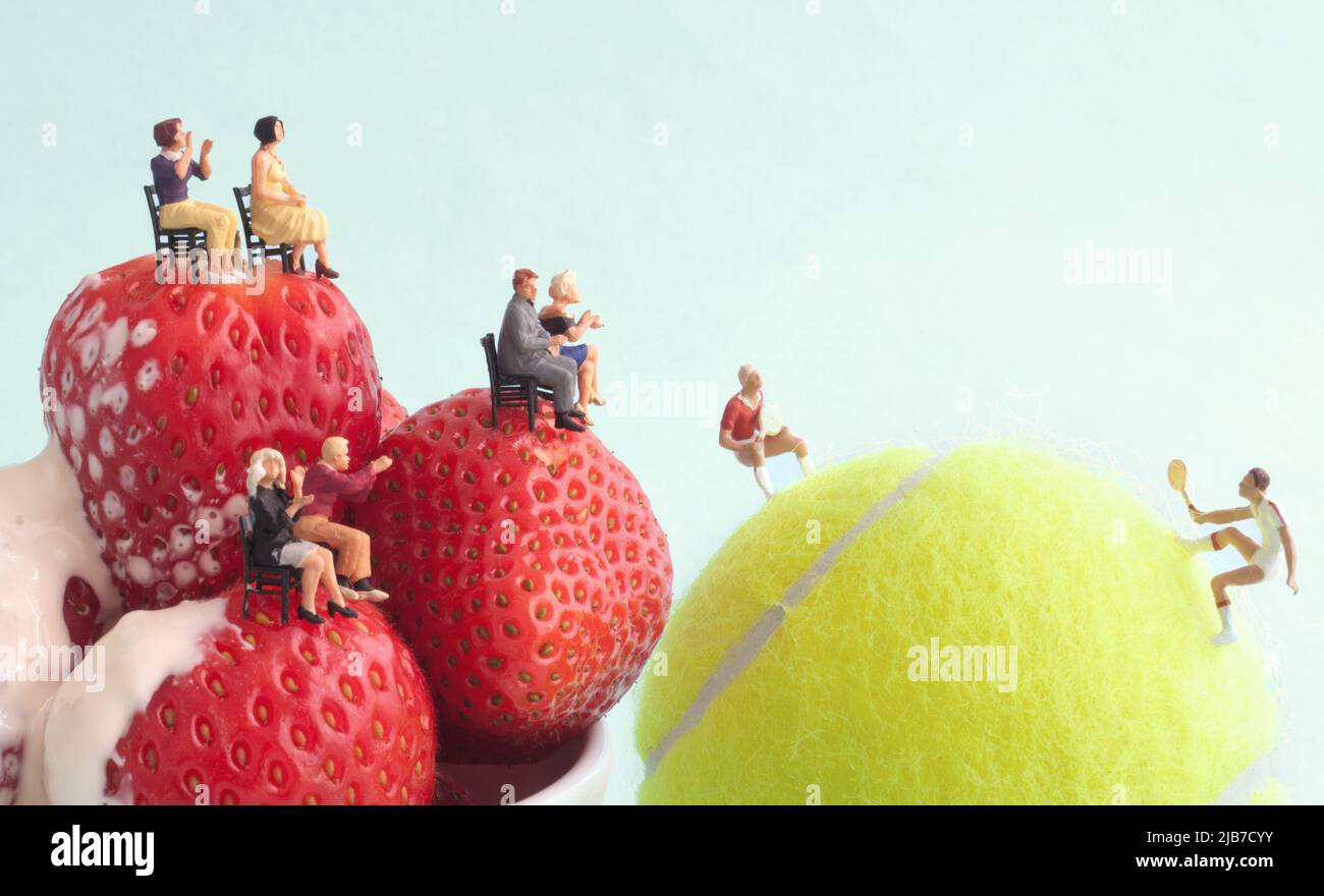 Miniature players on tennis ball with onlooking seated spectators on strawberries and cream, summer grass, wimbledon tennis concept Stock Photo
