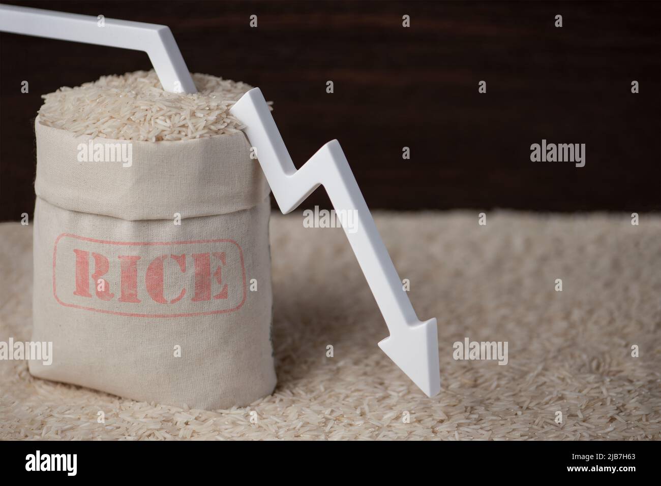 Rice harvest. Poor agricultural crops, food shortages, world hunger. A bag of rice on a brown background with a white arrow pointing down. Stock Photo