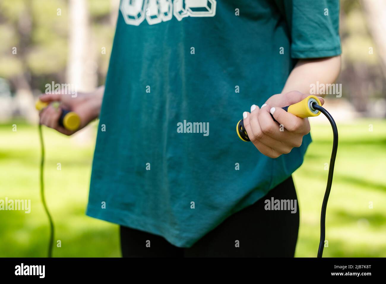Close up view of young redhead woman wearing green tee standing on city park, outdoor flat stomach with a skipping rope in her hands at waist level. H Stock Photo