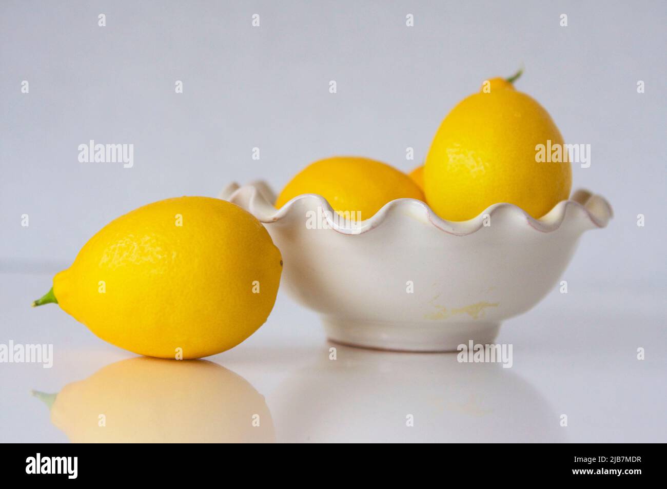 Bright yellow lemons in decorative bowl on white background. Stock Photo