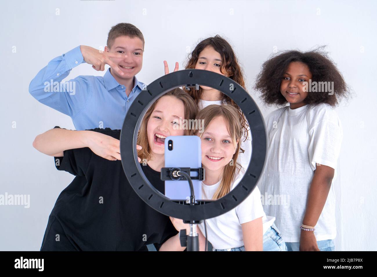 Four Teen girls and one boy smiling and shoots a video. selfies. The phone is mounted on a tripod and the ring lamp shines. Teenagers and social netwo Stock Photo