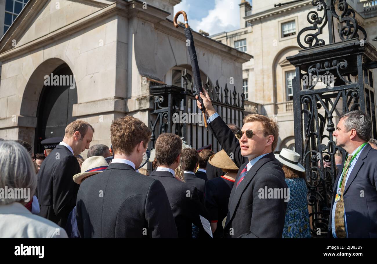 A man in a suit with a British Army Horse Guards regimental tie holds up an umbrella in a crowd of VIPS waiting to enter Horse Guards Parade for the P Stock Photo