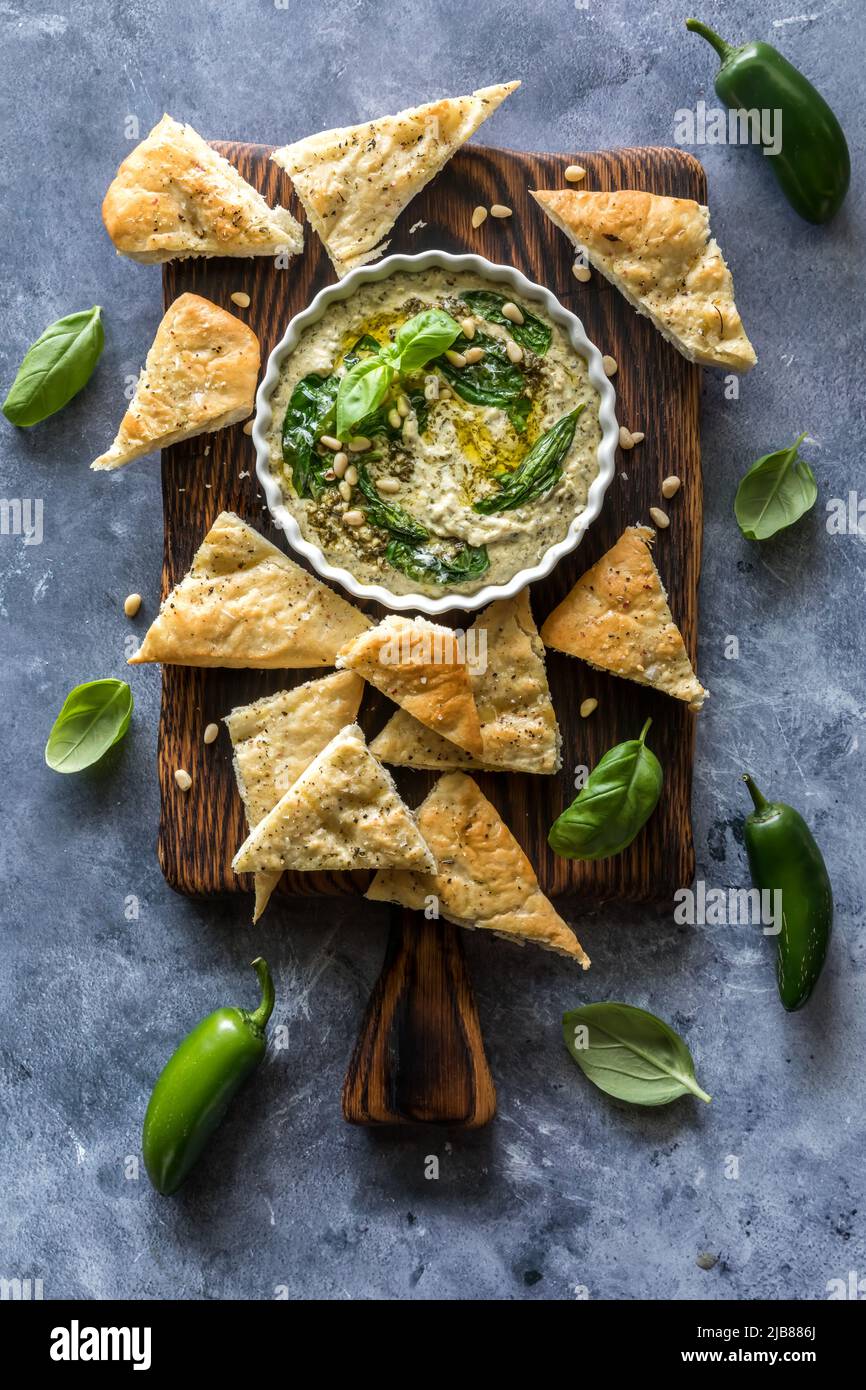 Pesto hummus with pita triangles on a wooden board, ready for snacking. Stock Photo