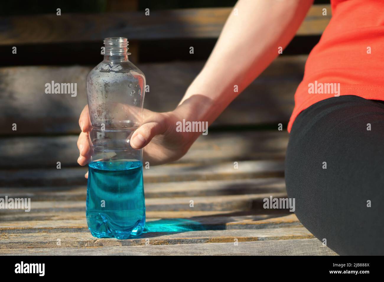 Girl is resting on a park bench holding a blue isotonic drink in her hand. Stock Photo