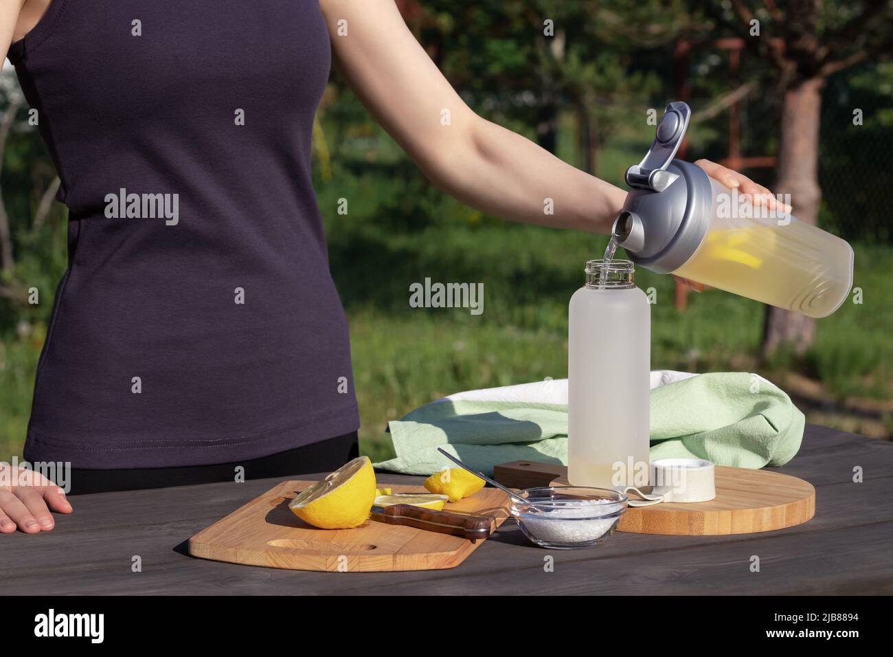 Girl makes a fresh homemade isotonic drink from natural ingredients - salt, lemon and mineral water. Stock Photo