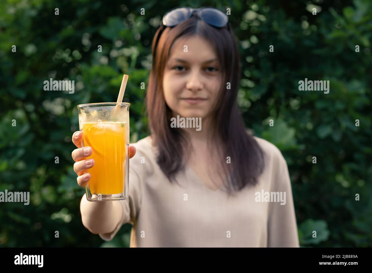 Beautiful girl holds out a glass with a fresh orange summer cocktail, selective focus. Stock Photo