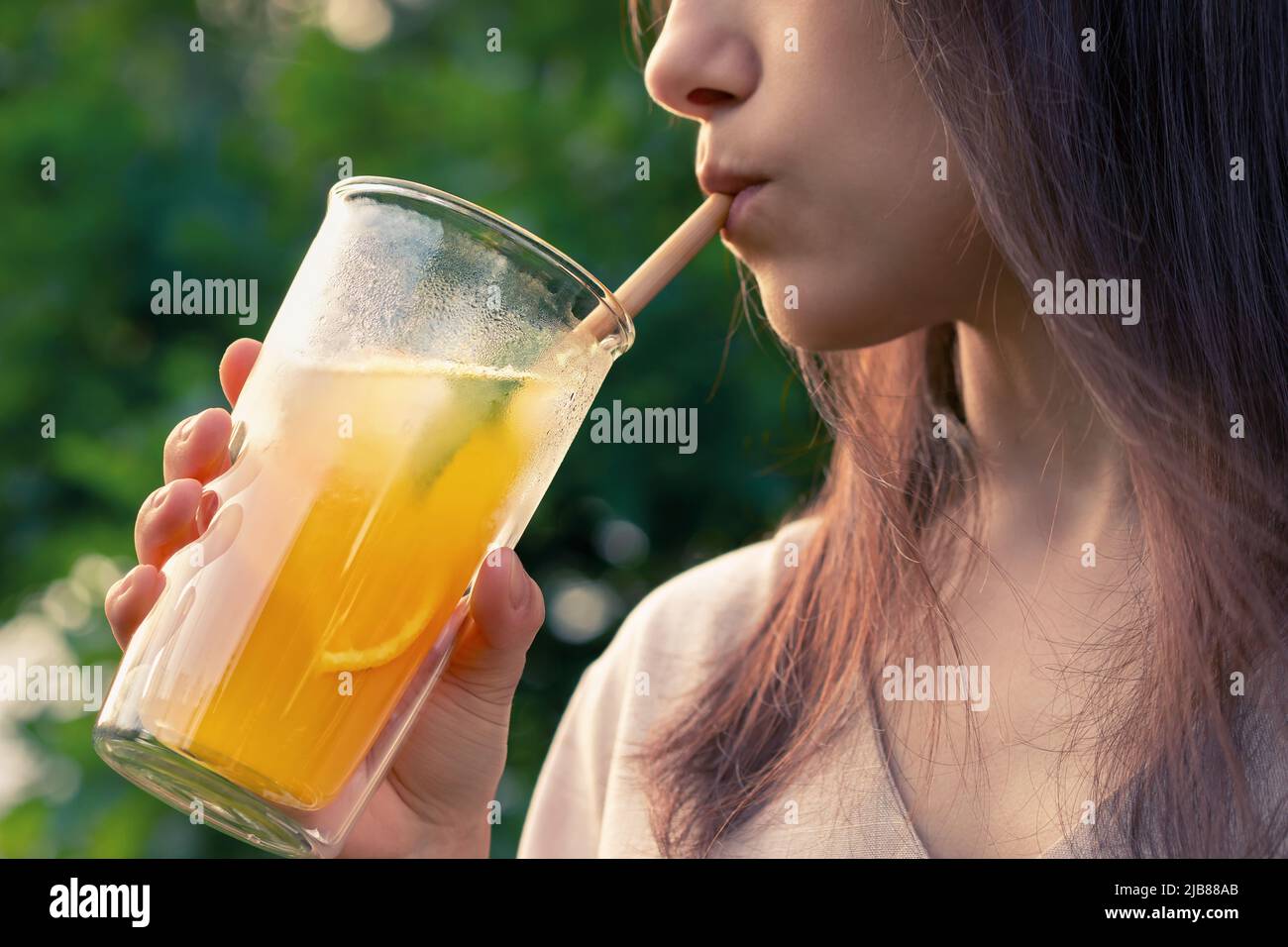 Girl drinks from a glass with fresh orange summer cocktail, close-up, selective focus. Stock Photo