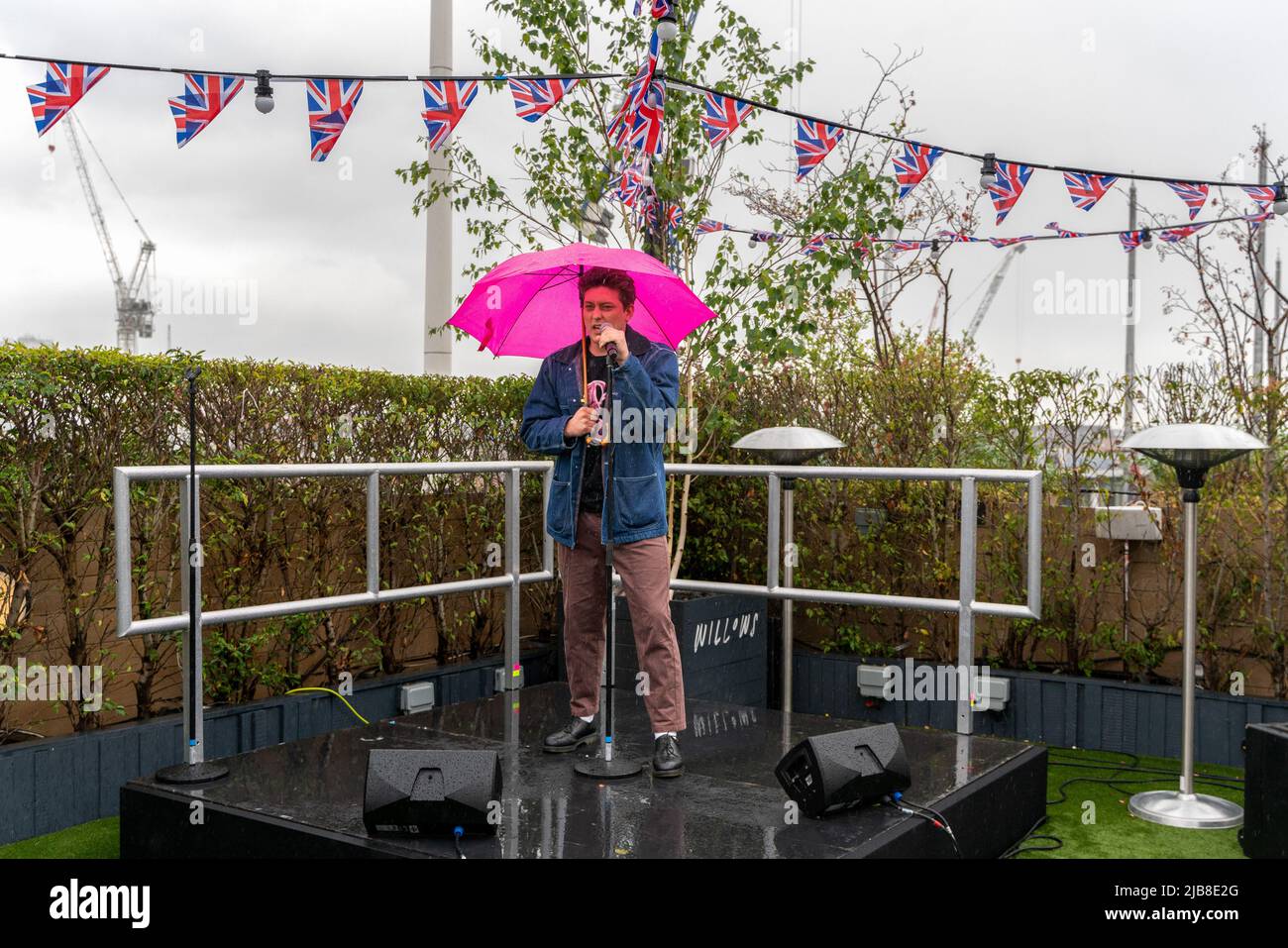 Tom Francis who plays Romeo in West End Musical '& Juliet' sings in the rain on John Lewis rooftop. The Second performance in the 'Sing it from the Rooftops' series. Surprise, pop-up performances was from & Juliet The Musical, lead actors Miriam-Teak Lee (Juliet) and Tom Francis (Romeo) performed songs from the multi-award-winning musical at Willows on the Rooftop of the iconic John Lewis and Partnersí Oxford Street store. 'Sing it from the Rooftops' is a teaser campaign for West End Live, to pre-promote Europe's biggest free musical theatre festival which returns on Saturday 25 & Sunday 26 Ju Stock Photo