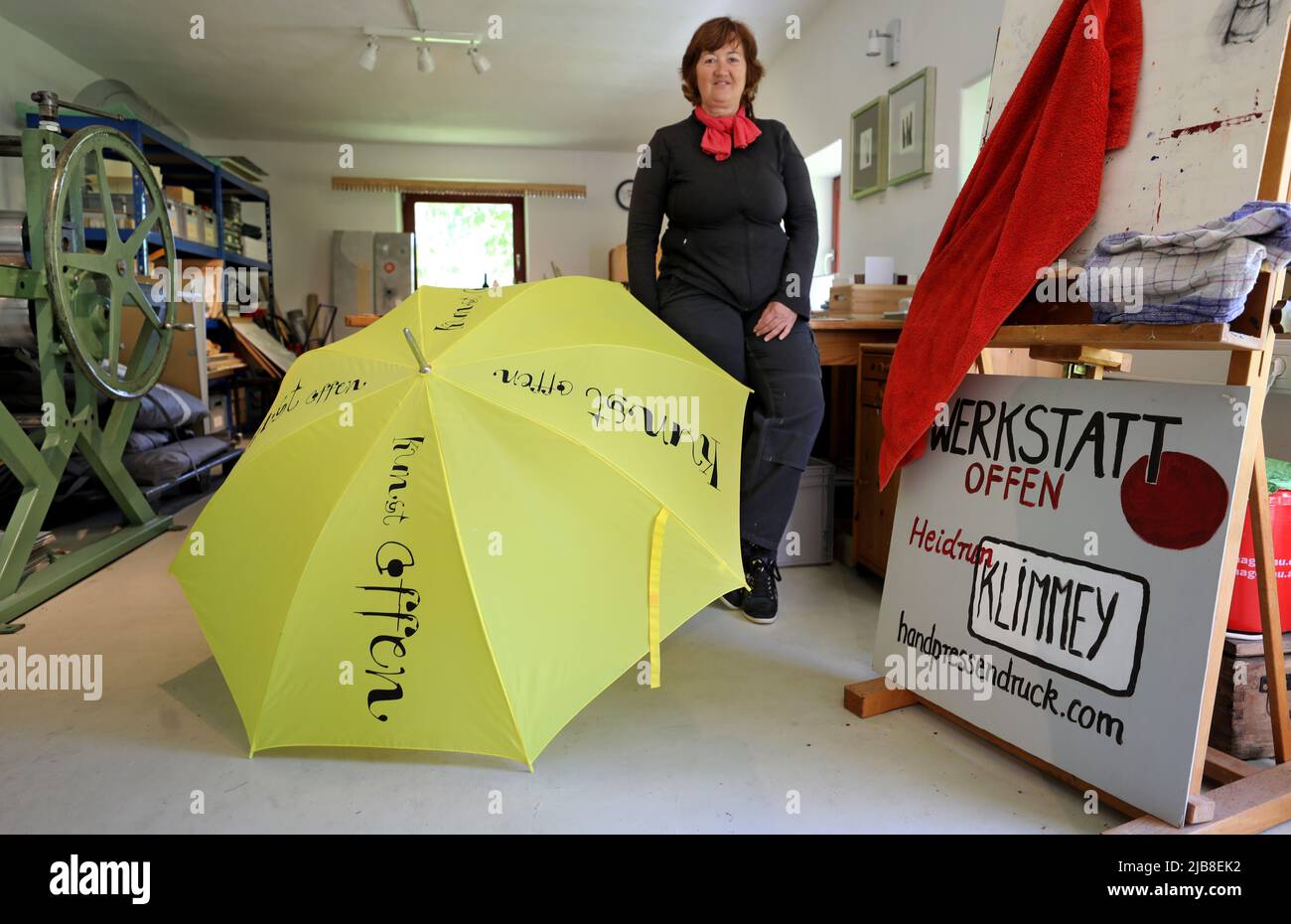 Rothen, Germany. 03rd June, 2022. Heidrun Klimmey stands in her workshop at Rothener Hof, where she makes prints. A yellow umbrella with the inscription 'Kunst offen' (Art Open) invites visitors to view the workshop and an exhibition 'Zwischen uns' (Between Us) by five female artists. During the nationwide 'Art Open' campaign, some 900 artists at more than 500 locations will open their workshops and studios to visitors on the Whitsun weekend of June 4-6, 2022. Credit: Bernd Wüstneck/dpa/Alamy Live News Stock Photo