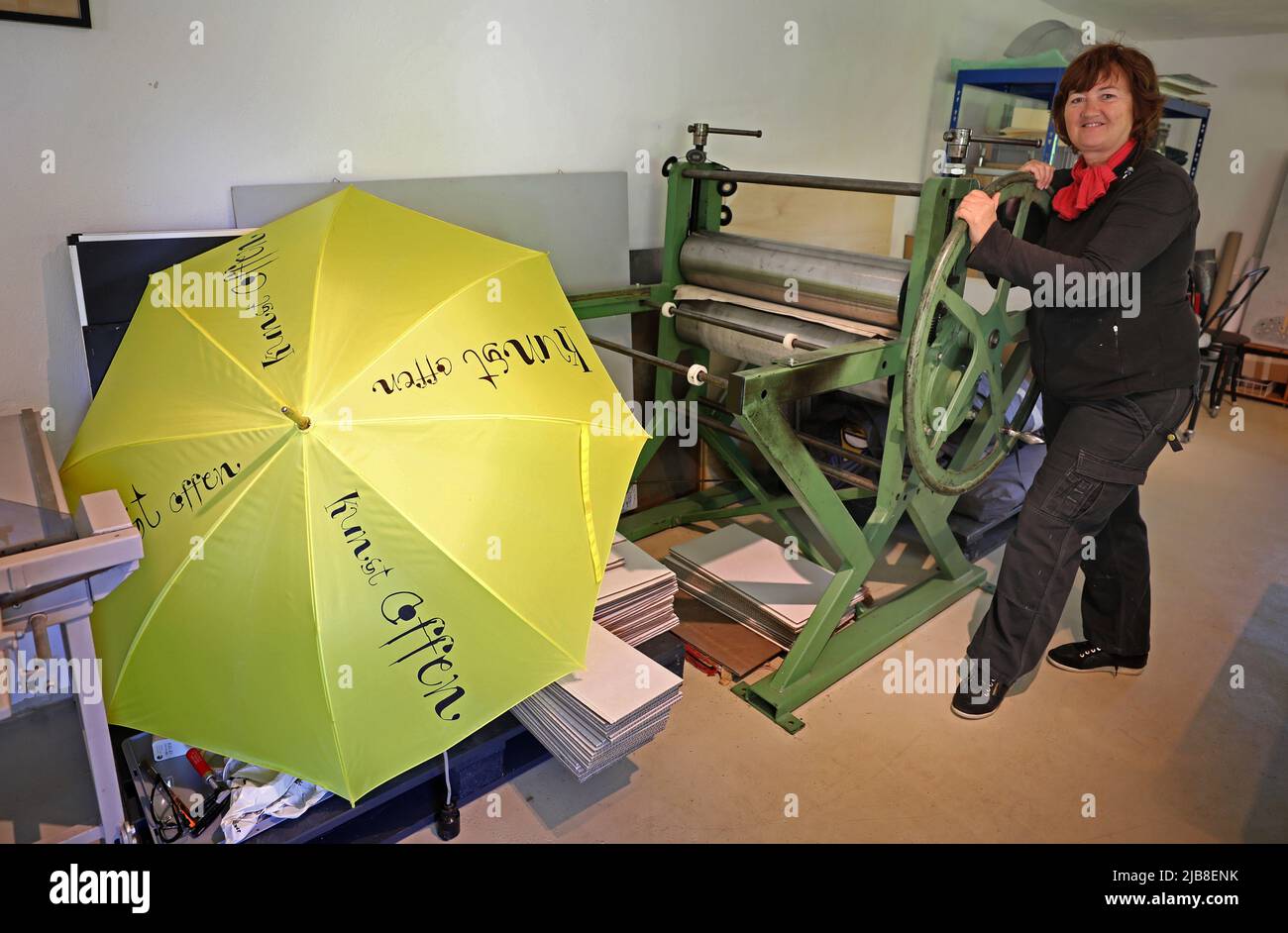 Rothen, Germany. 03rd June, 2022. Heidrun Klimmey stands in her workshop at Rothener Hof, where she makes prints. A yellow umbrella with the inscription 'Kunst offen' (Art Open) invites visitors to view the workshop and an exhibition 'Zwischen uns' (Between Us) by five female artists. During the nationwide 'Art Open' campaign, some 900 artists at more than 500 locations will open their workshops and studios to visitors on the Whitsun weekend of June 4-6, 2022. Credit: Bernd Wüstneck/dpa/Alamy Live News Stock Photo
