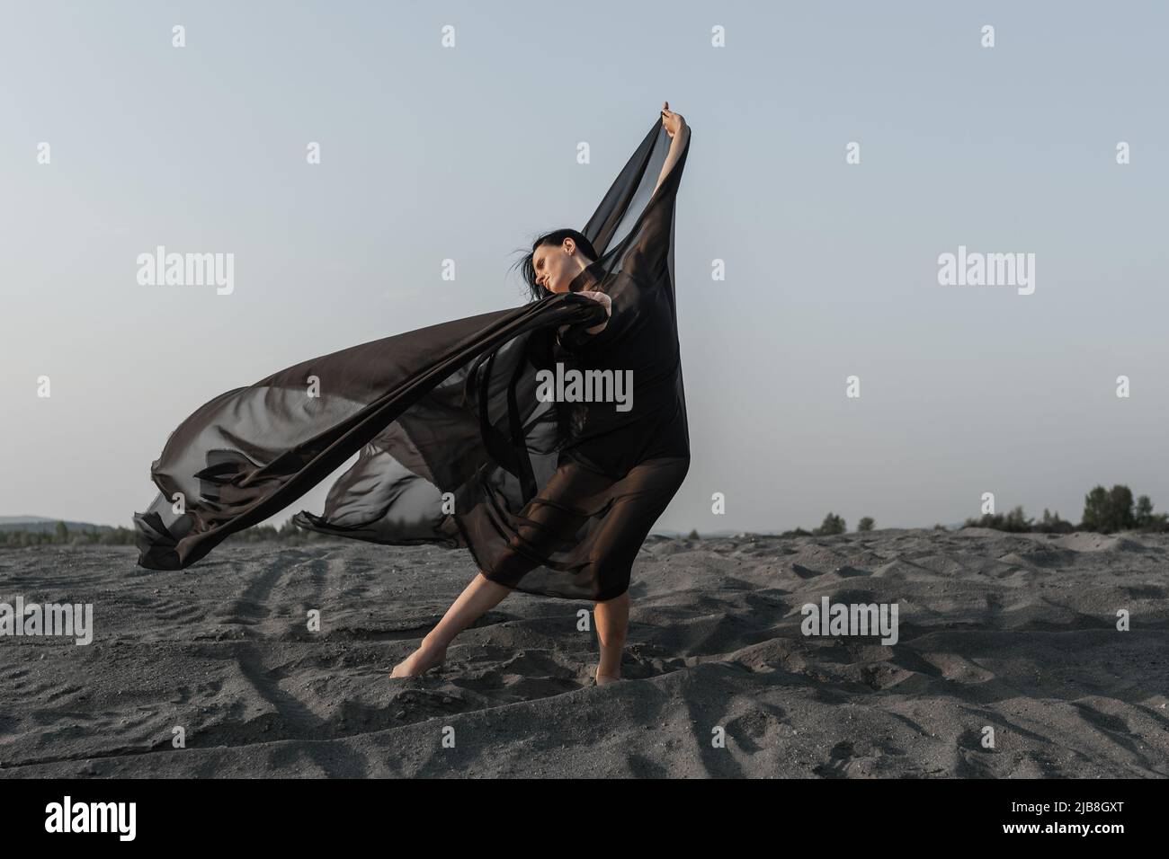 Woman in black with flying fabric dancing on the sand dune Stock Photo
