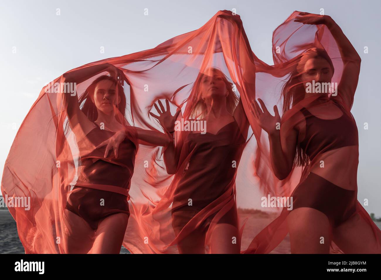 Three girls in red flowing fabric romantic pose and dance on sand dune Stock Photo