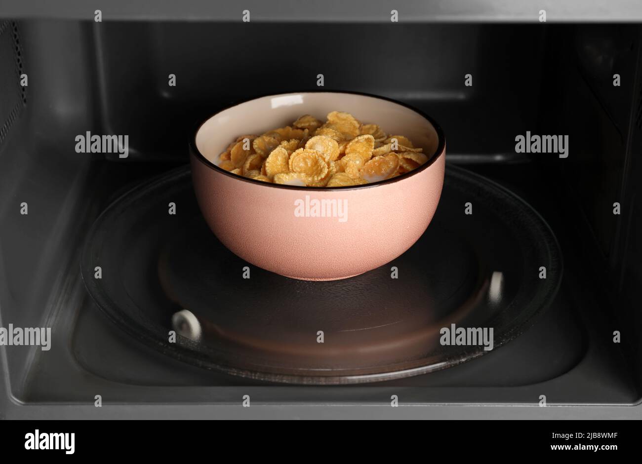 Bowl of tasty corn flakes with milk in microwave oven, closeup Stock