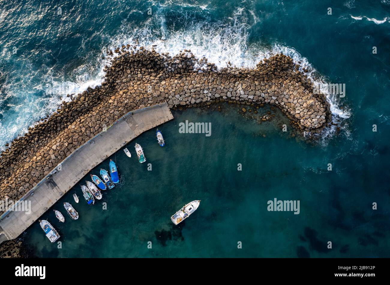 Aerial drone view of fishing boats moored at harbor at breakwater. Stormy waves at sea Stock Photo