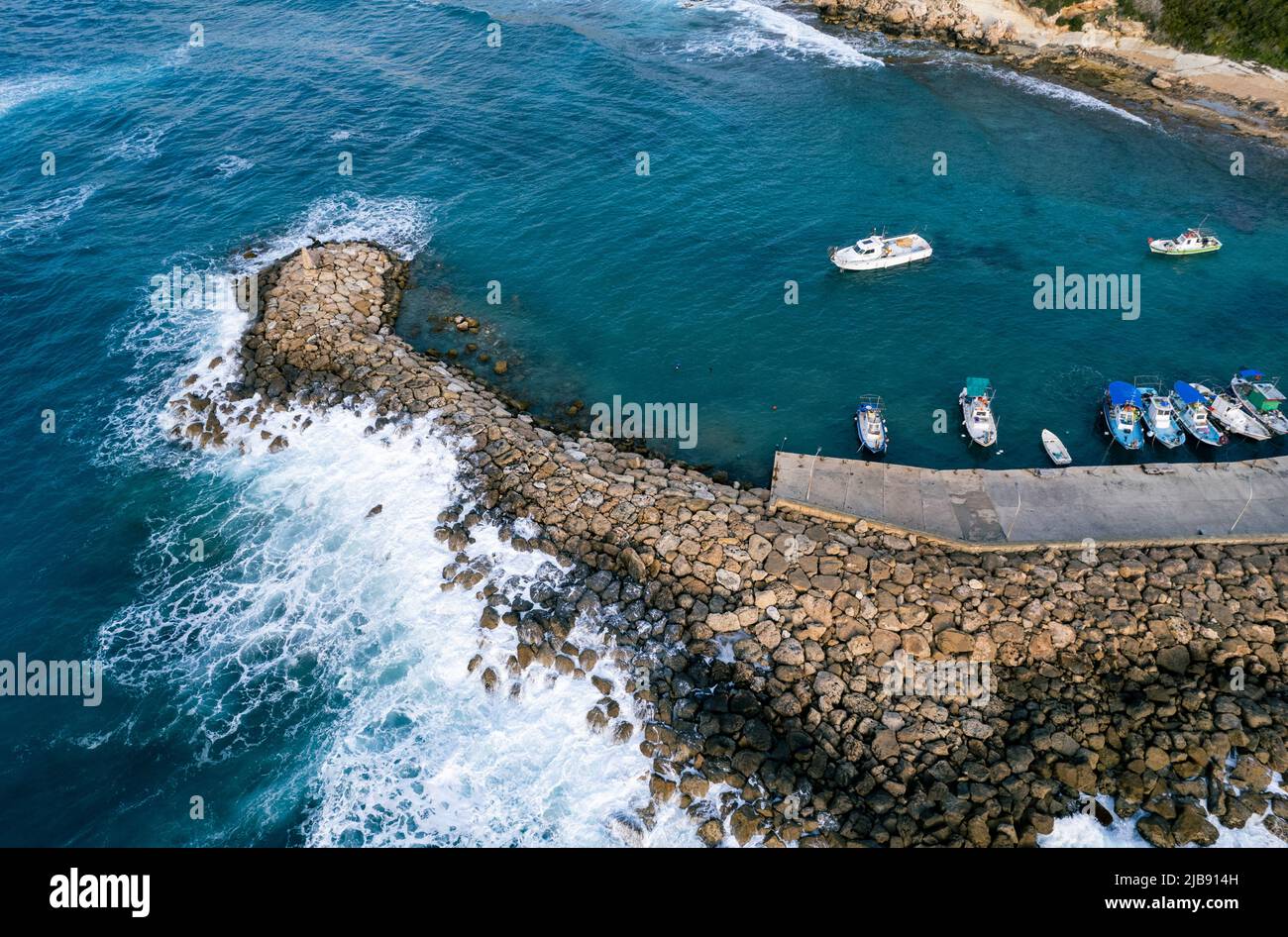 Aerial drone view of fishing boats moored at harbor at breakwater. Stormy waves at sea Stock Photo