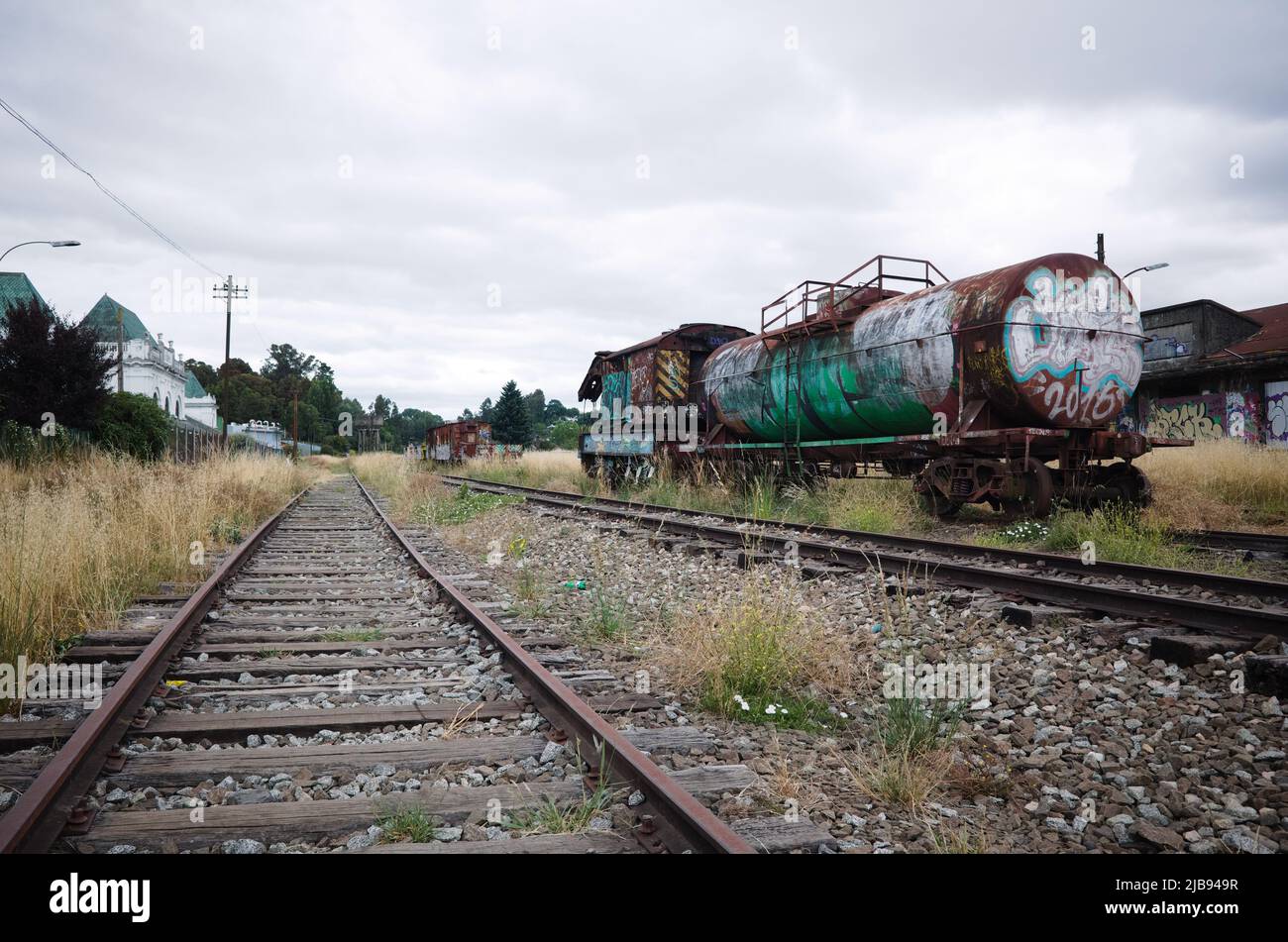 Osorno, Chile - February, 2020: Abandoned rail wagon with cistern covered in graffiti on railway tracks. Old railway station of Osorno on left Stock Photo