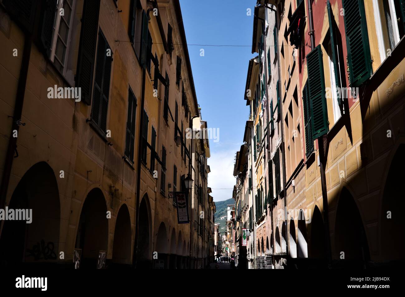 Chiavari, Italy - May, 2022: Narrow street with typical Italian buildings with wooden shutters on windows. Streak of blue sky between two buildings Stock Photo