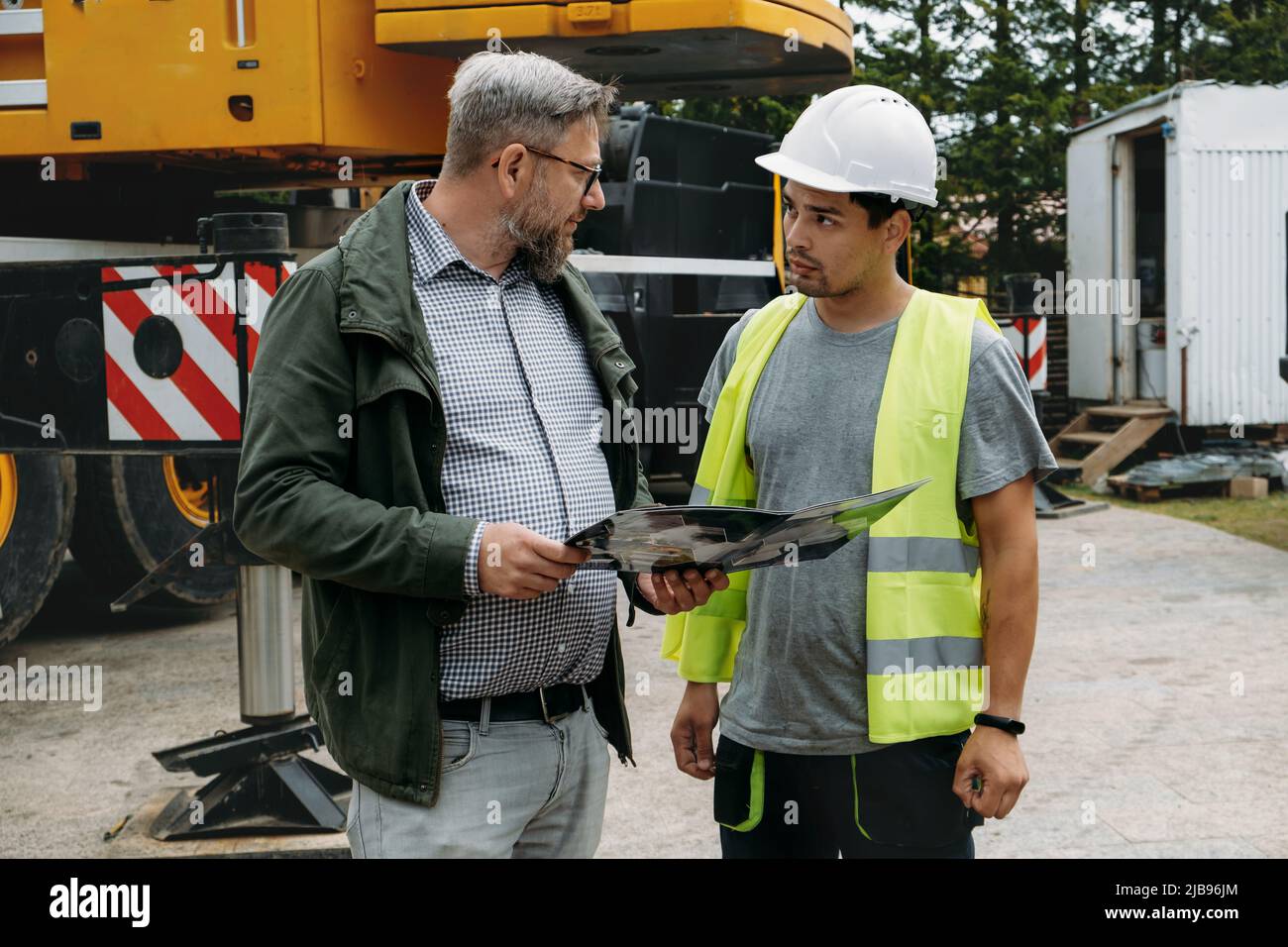 Foreman and customer or client agree about future building work on construction site. architect discussing project with builder over crane vehicle Stock Photo