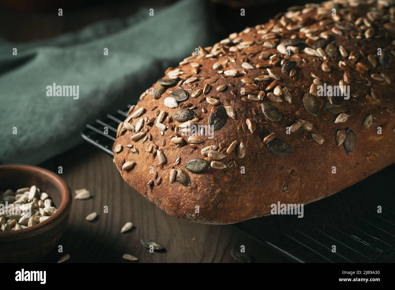 Loaf of homemade whole grain bread with seeds cool down on a wire rack on a wooden table. Stock Photo