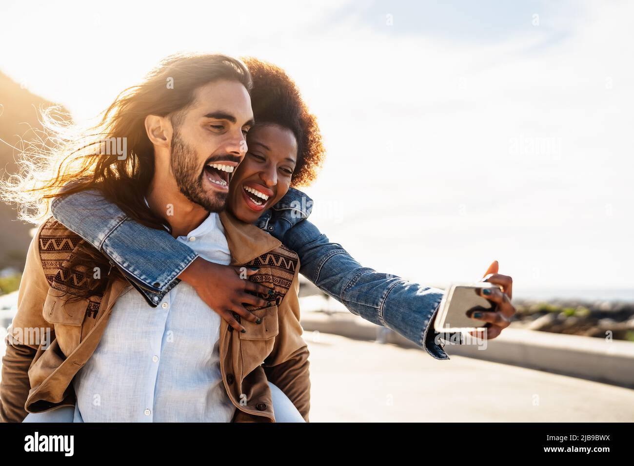 Happy multiracial couple having fun taking selfie with mobile smartphone during vacations - Youth people love and social relationship concept Stock Photo