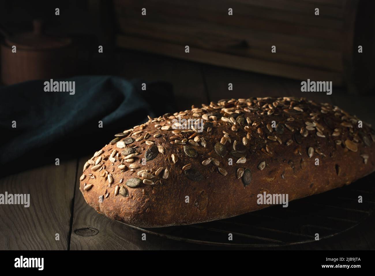 Loaf of homemade whole grain bread with seeds cool down on a wire rack on a wooden table. Stock Photo