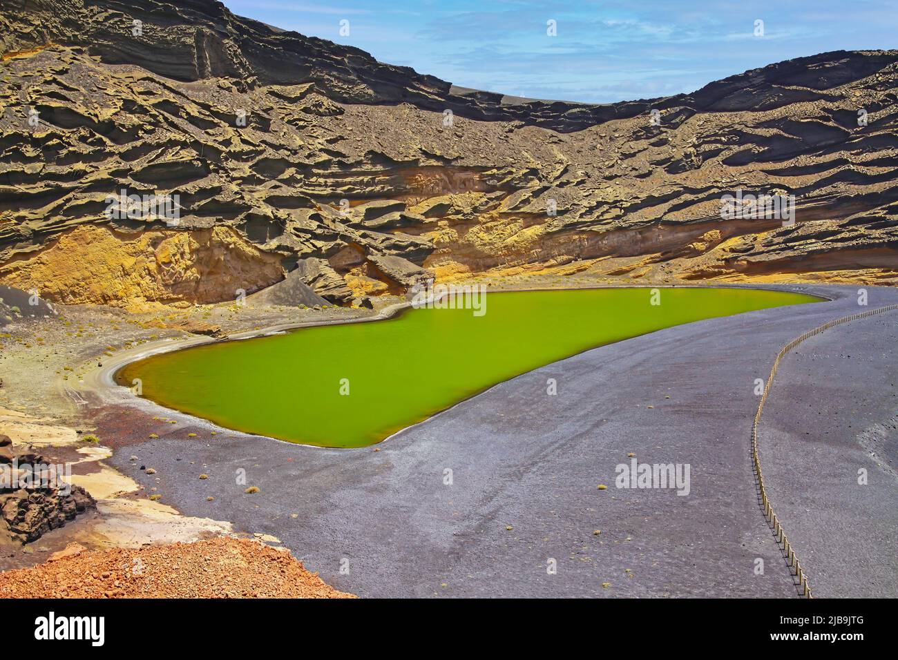 Beautiful secluded lagoon valley, red rocks, deep green lake (Lago verde), black lava sand, impressive rugged sharp steep cliffs - El Golfo, Lanzarote Stock Photo