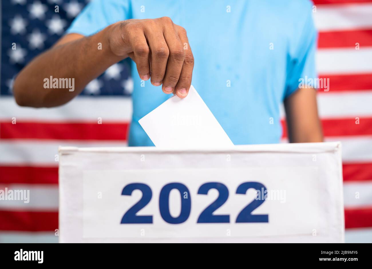Man placing ballot paper into 2022 ballot box in front of american flag - concept of 2022 midterm US election, voting and democracy Stock Photo