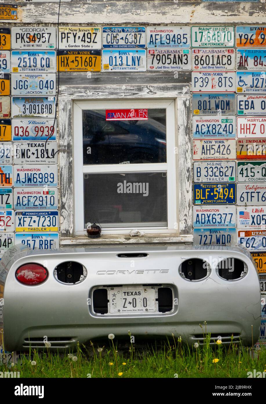 car license plates from different states and a corvette car rear end underneath a window on the