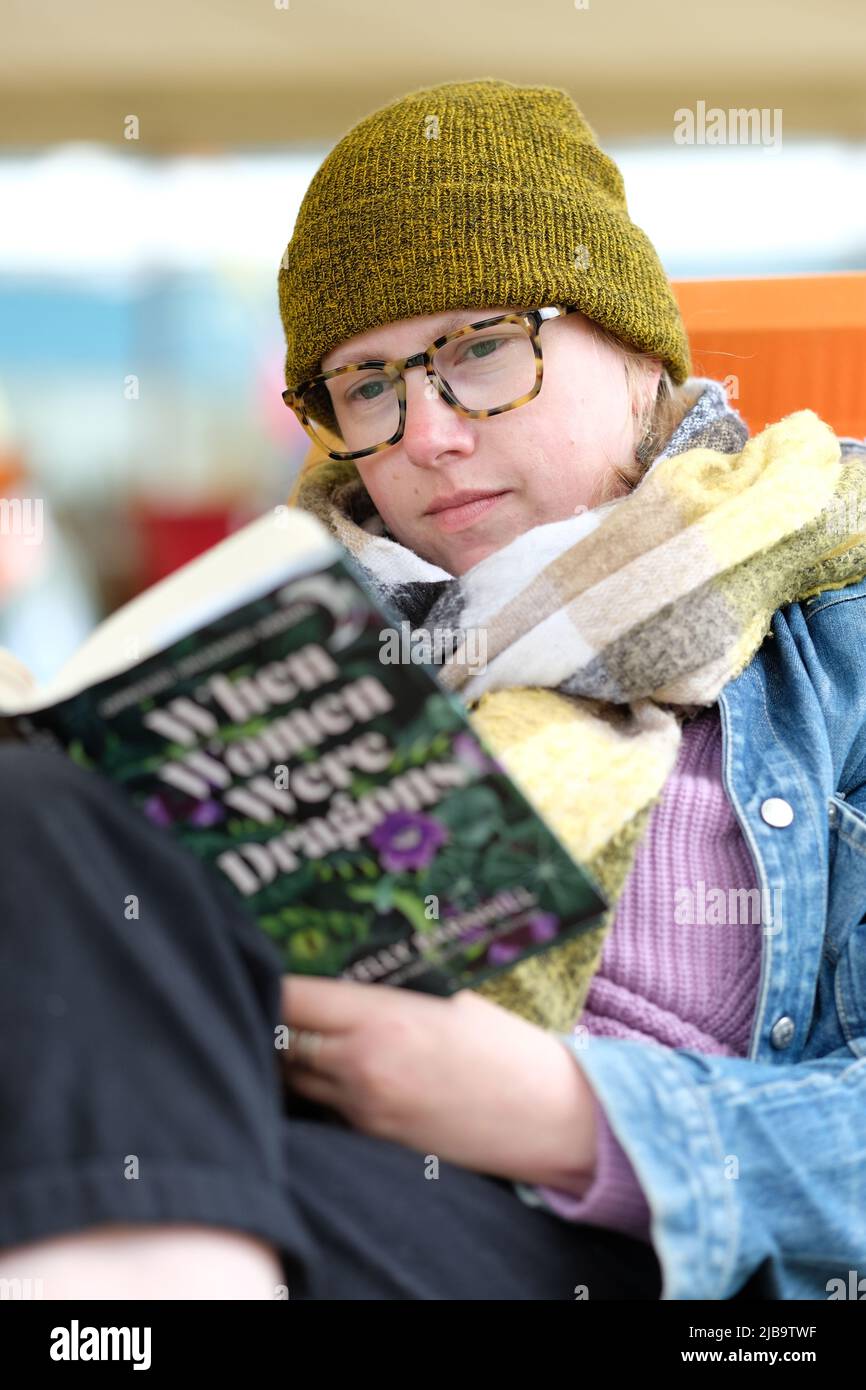 Hay Festival, Hay on Wye, Wales, UK – Saturday 4th June 2022 – Woolly hat weather at Hay - A visitor to Hay enjoys a chance to read on the Festival Lawns between events at the first in person Hay Festival since 2019. Photo Steven May / Alamy Live News Stock Photo