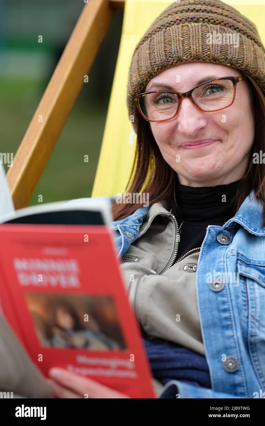 Hay Festival, Hay on Wye, Wales, UK – Saturday 4th June 2022 – Woolly hat weather at Hay - A visitor to Hay enjoys a chance to read on the Festival Lawns between events at the first in person Hay Festival since 2019. Photo Steven May / Alamy Live News Stock Photo