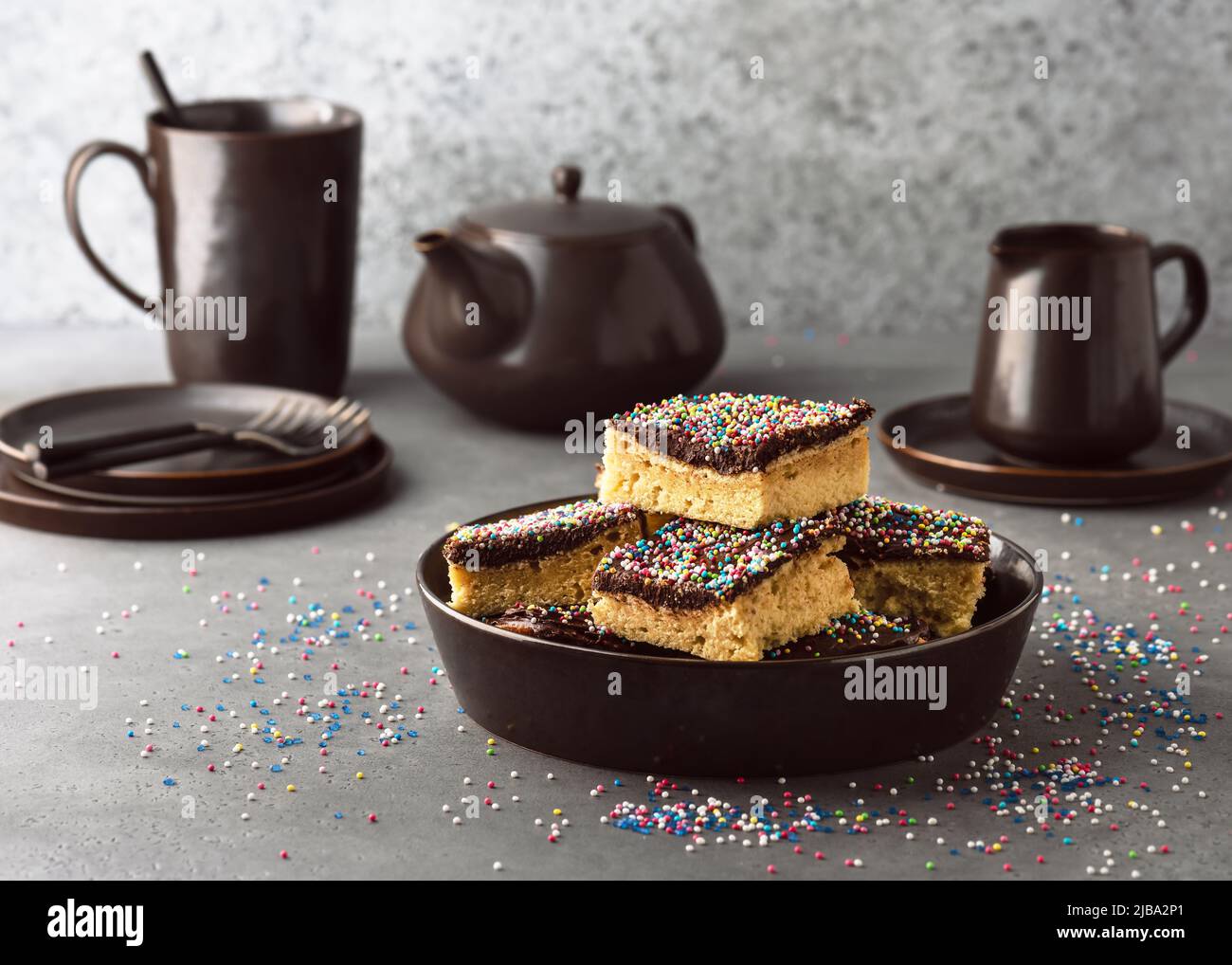 Delicious homemade cake with dark chocolate icing and colorful sugar sprinkle served on one plate. Rustic style. Selective focus. Copy space. Stock Photo
