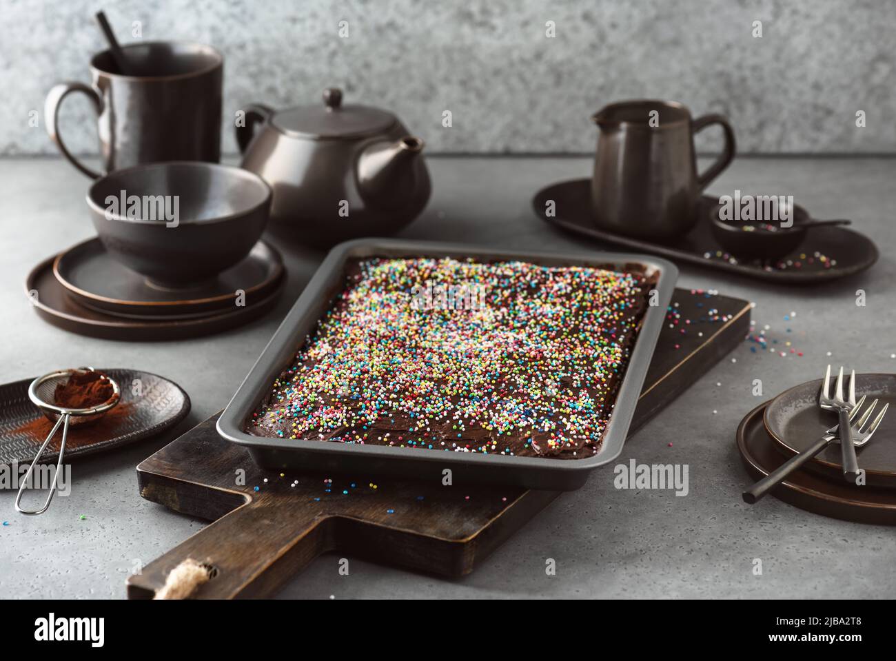 Fresh baked cake covered with dark chocolate icing and colorful sprinkles in a baking pan. Homemade sweet food concept. Selective focus. Stock Photo