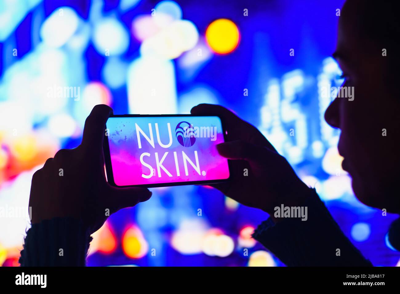 In this photo illustration, a silhouetted woman holds a smartphone with the Nu Skin Enterprises logo displayed on the screen. Stock Photo