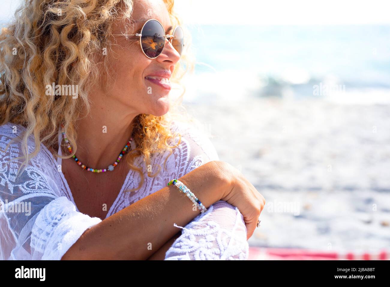 Close up side portrait of woman smiling and enjoying sun at the beach in summer holiday vacation. Tourist female people with sunglasses and blonde sur Stock Photo