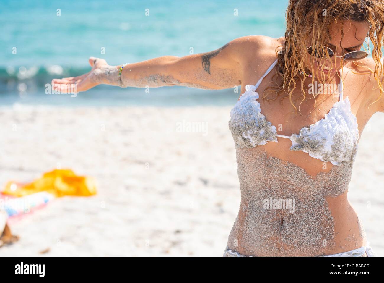 Overjoyed young woman sith sand on the body have fun at the beach. Female enjoying summer sun and holiday vacation. Leisure activity people outdoor fu Stock Photo