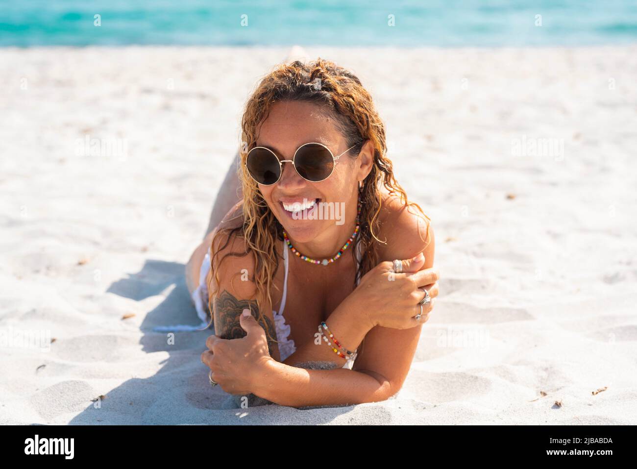 Portrait of cheerful young adult woman laying at the beach on white sand. Tropical summer holiday vacation. Relaxed female people smile and enjoy the Stock Photo