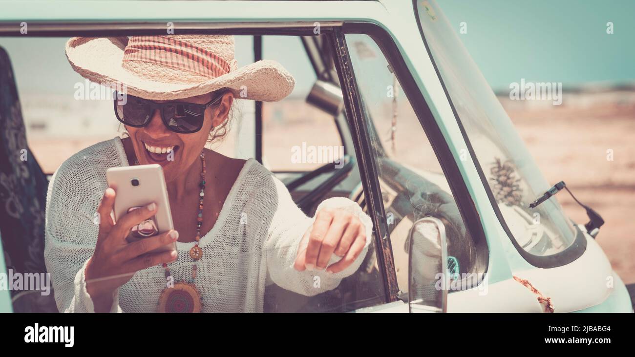 Happy young woman have fun using mobile phone sitting on a classic van. Travel and freedom people lifestyle. Concept of summer holiday vacation. Prett Stock Photo