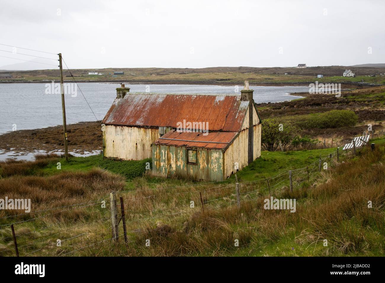 An elderly and dilapidated corrugated  tin cottage with stone stacks in Berneray Harbour, beyond North Uist in the Outer Hebrides, Scotland Stock Photo