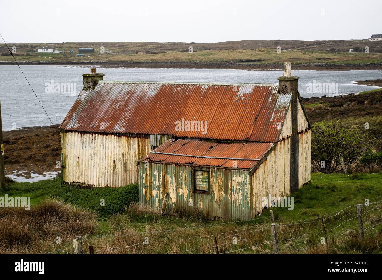 An elderly and dilapidated corrugated  tin cottage with stone stacks in Berneray Harbour, beyond North Uist in the Outer Hebrides, Scotland Stock Photo