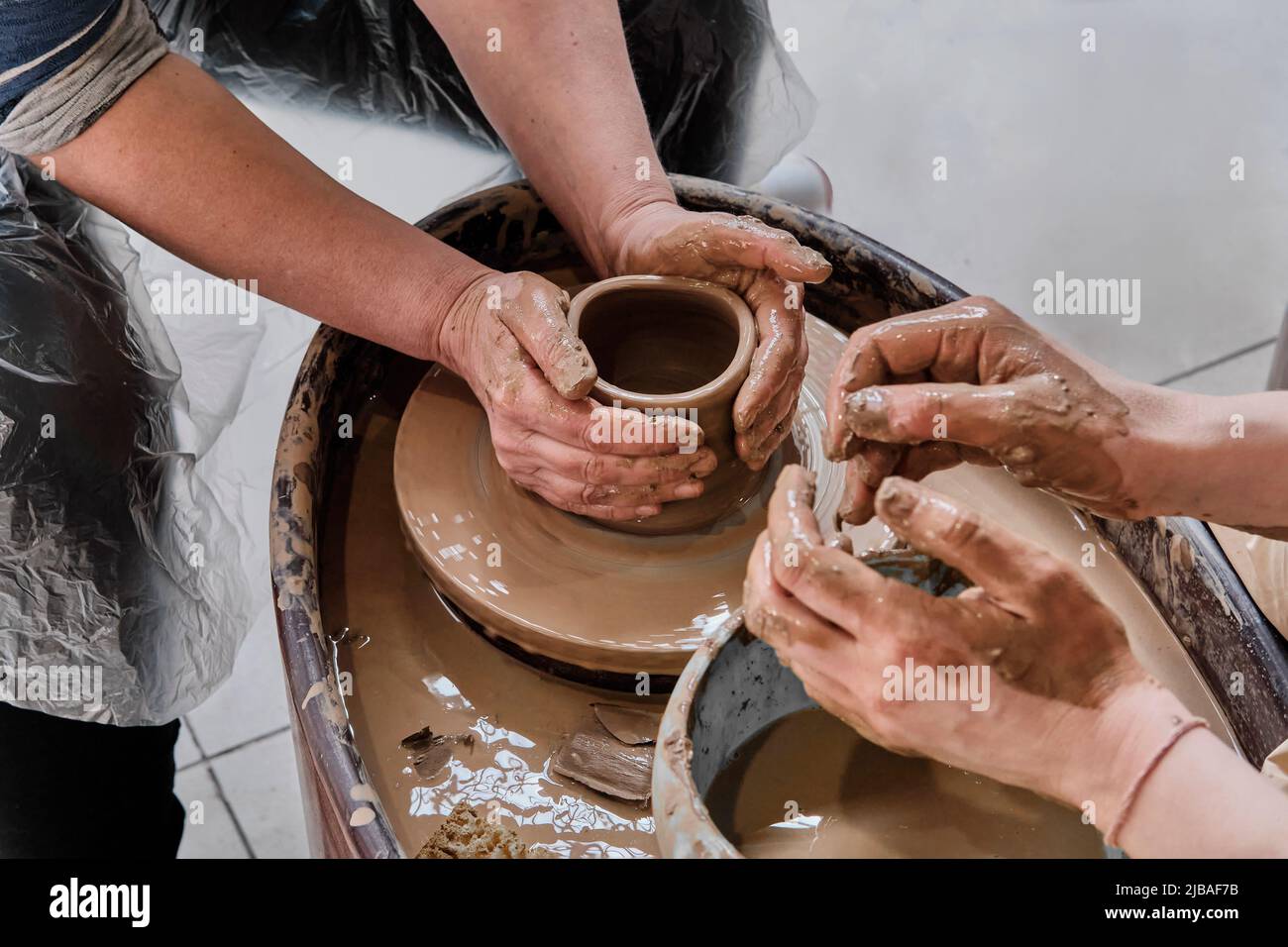 Hands of senior woman and girl sculpting clay vase on potter's wheel at