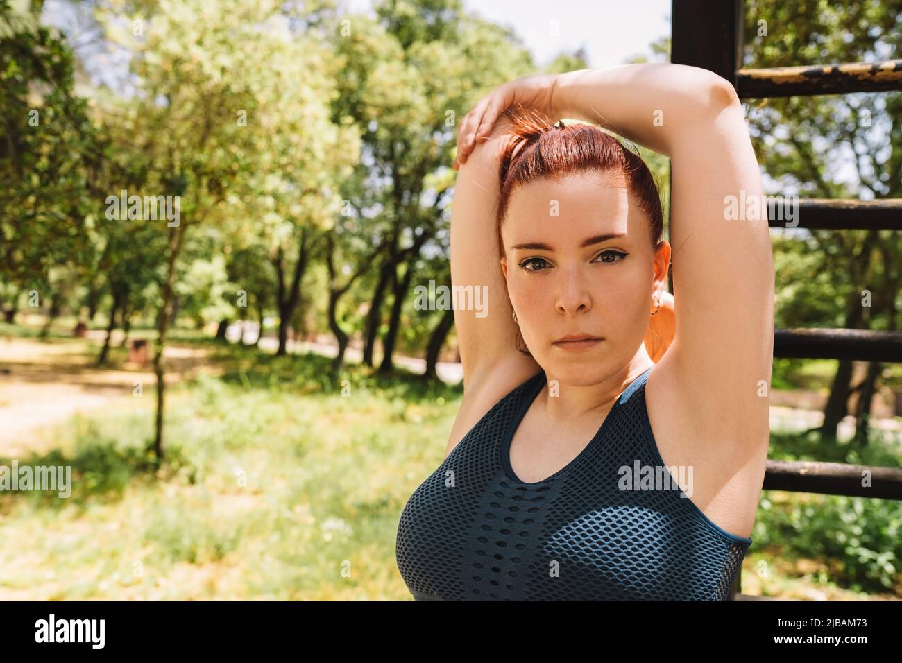young athletic woman looking at camera doing stretching exercises to tone her body. athletic person playing sport outdoors. health and wellness Stock Photo