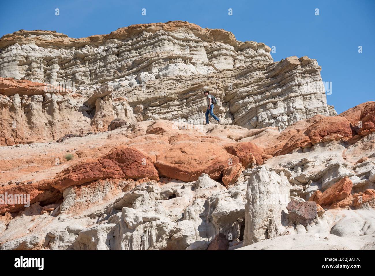A man explores a red sandstone cliff layer in Hagen Canyon Natural Preserve at Red Rock Canyon State Park in California, a scenic desert hiking trail. Stock Photo