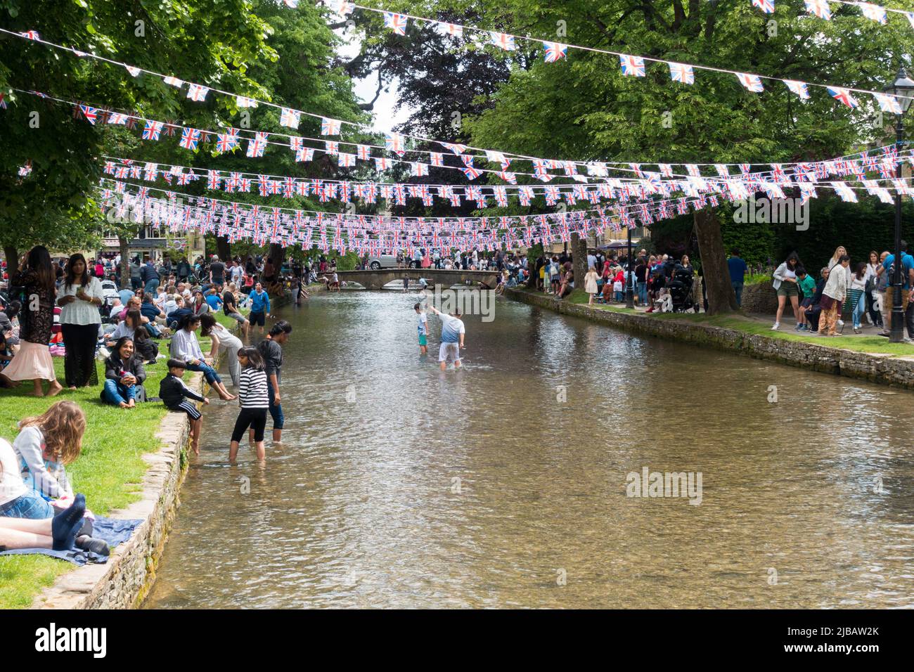 Large crowd on the banks of River Windrush in Bourton enjoying sunny